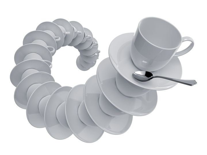 A spiral of white teacups and saucers forms a circular pattern, with one cup and spoon resting on top.