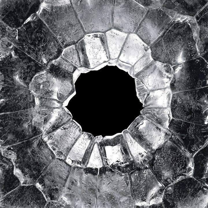 A shattered glass surface reveals a dark, circular hole surrounded by jagged, translucent shards.