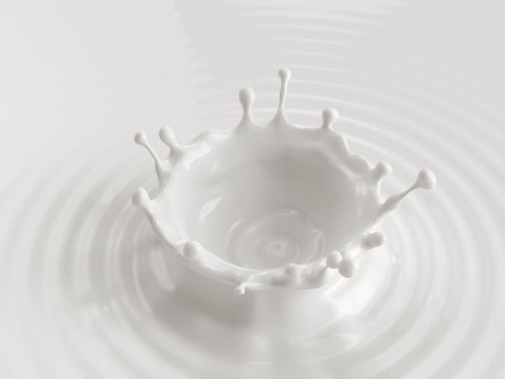 A white liquid splashes upward, forming a crown shape with droplets, creating ripples on a smooth surface.