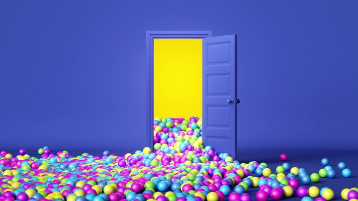 A blue door opens and many little multicolored balloons and balls fall out. A bright yellow light shines from the door. 3D animation of a party or celebration